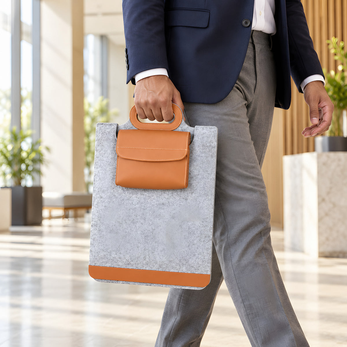 Man carrying the grey Unfold sleeve by its tan handle through an office lobby